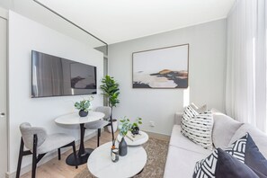Ein modernes Wohnzimmer mit einer Couch, einem Esstisch mit Stühlen, einem Couchtisch und einem an der Wand befestigten Fernseher.