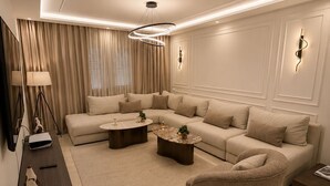 Una sala de estar moderna con un sofá modular, una mesa de centro redonda, una lámpara de pie y un televisor sobre un mueble bajo.