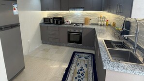 Una cocina moderna con gabinetes grises, un horno empotrado, un microondas y un lavamanos de acero inoxidable.
