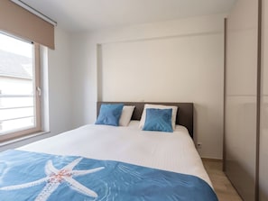 Ein Schlafzimmer mit einem Bett, zwei Kissen, einer Sterntausch-Decke, einem Fenster und einer Tür.
