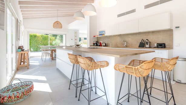Cozinha moderna com ilha central, banquetas e área de refeições com iluminação natural.