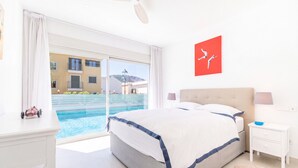Quarto com cama, mesa de cabeceira, abajur e vista para uma piscina.