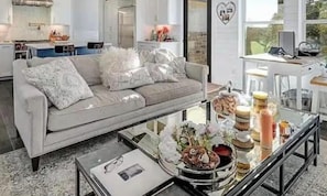 Een moderne woonkamer met een bank, salontafel en een keuken op de achtergrond.