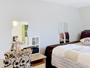 A bedroom with a bed, a nightstand, a chair, a mirror, and a shelf with decorative items.