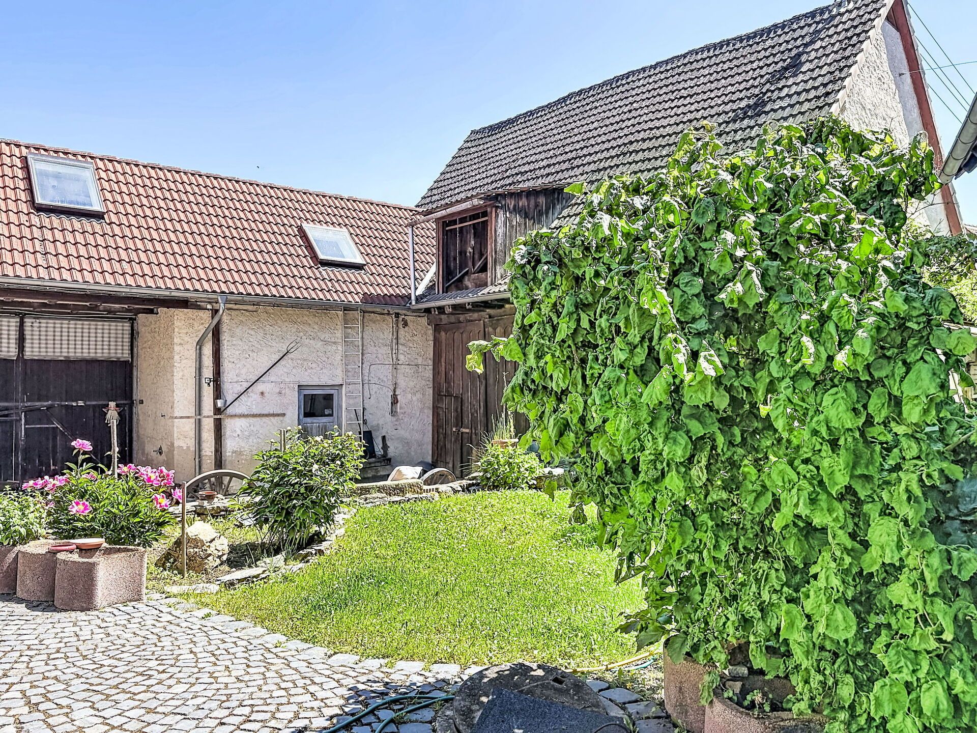 A building with a tiled roof, a garden with various plants, and a paved entrance.