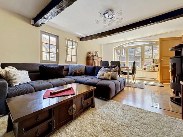 A living room with a dark-colored sofa, a wooden coffee table, and a fireplace. There are two windows and a door leading to an outdoor area.