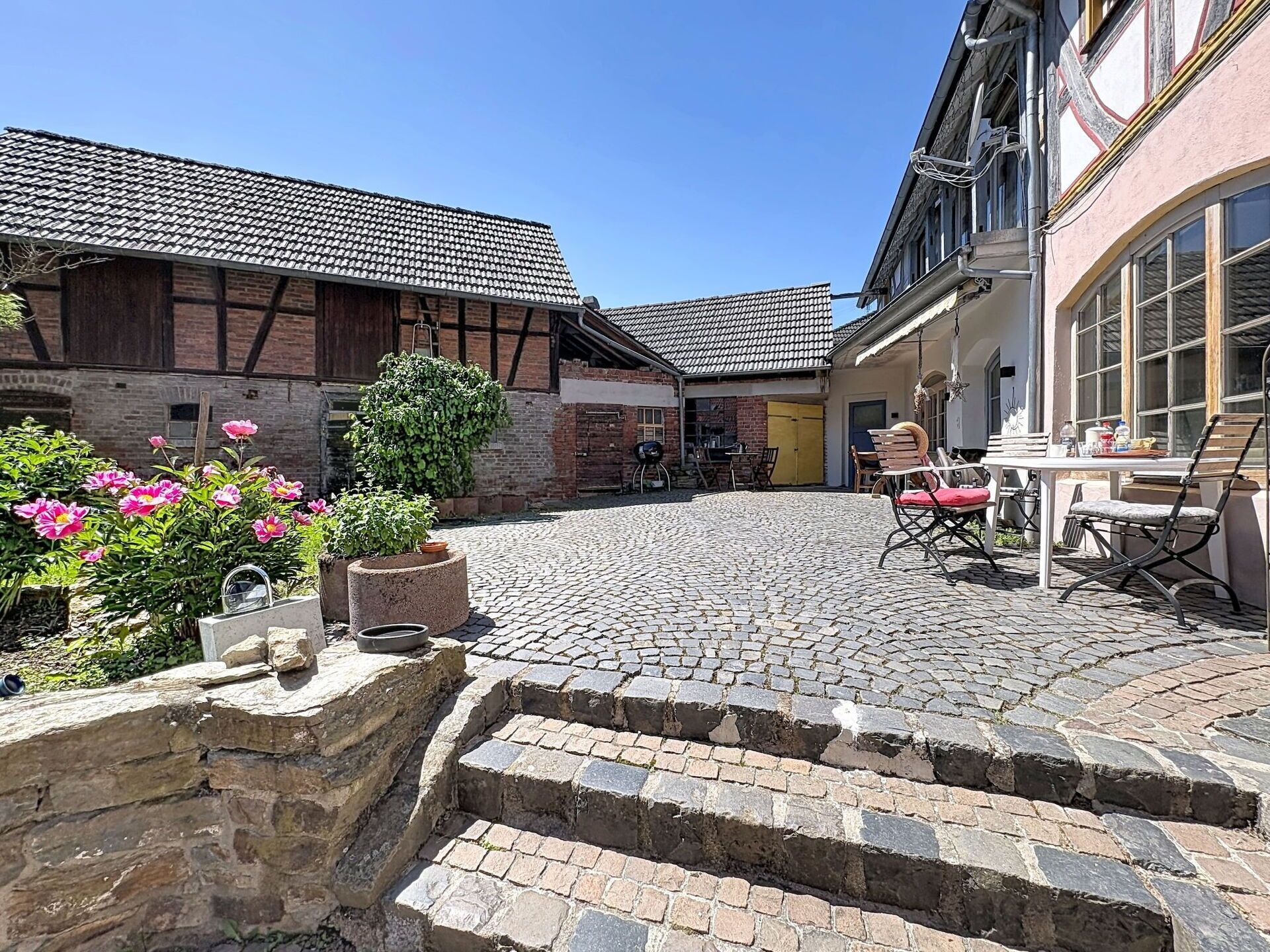 Ein Innenhof mit Kopfsteinpflaster, einer Steinsitzbank und einem Tisch mit Stühlen.