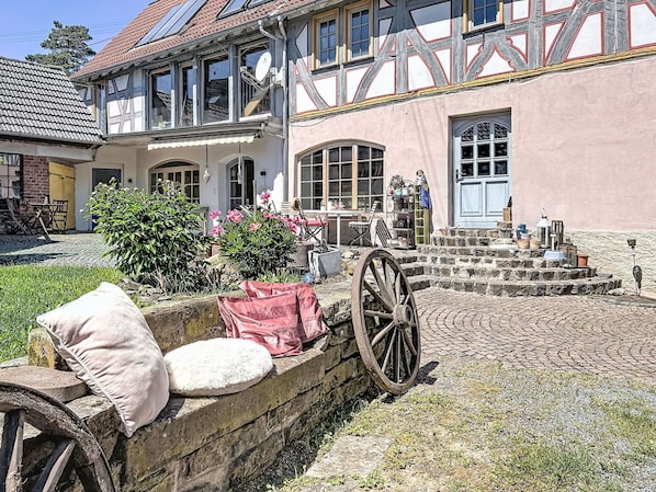 Una casa tradicional de entramado de madera con un patio, un muro de piedra y un carromato de madera.