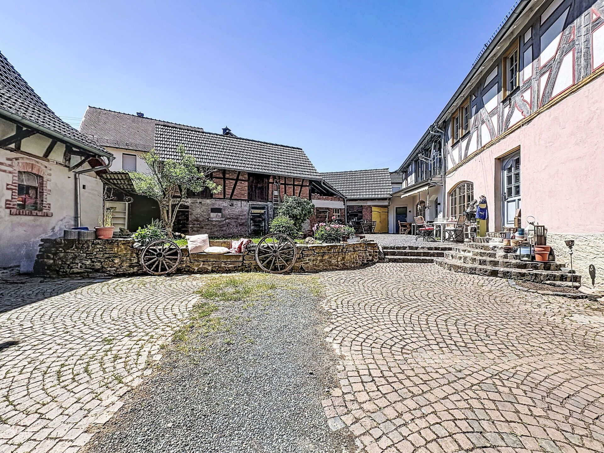 Ein Kopfsteinpflasterhof mit traditionellen Gebäuden, einer Steinmauer und einem hölzernen Wagen.