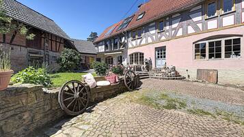 A traditional half-timbered building with a cobblestone courtyard, stone wall, and a large wooden wheel.