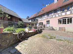 A traditional half-timbered building with a cobblestone courtyard, stone wall, and a large wooden wheel.