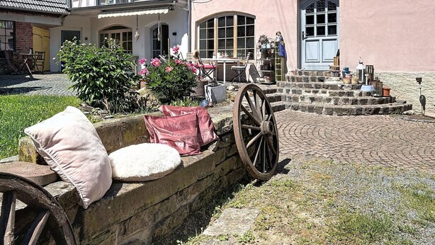 Une maison traditionnelle à colombages, dotée d’une cour, d’un mur en pierre et d’une charrette.