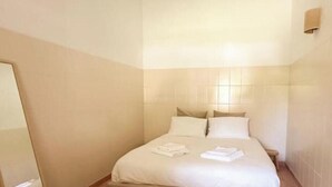 Une chambre d’hôtel avec un lit, une table de chevet et un luminaire fixé au mur.