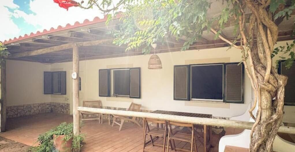 A covered patio with a table and chairs, a tree, and a building with windows.