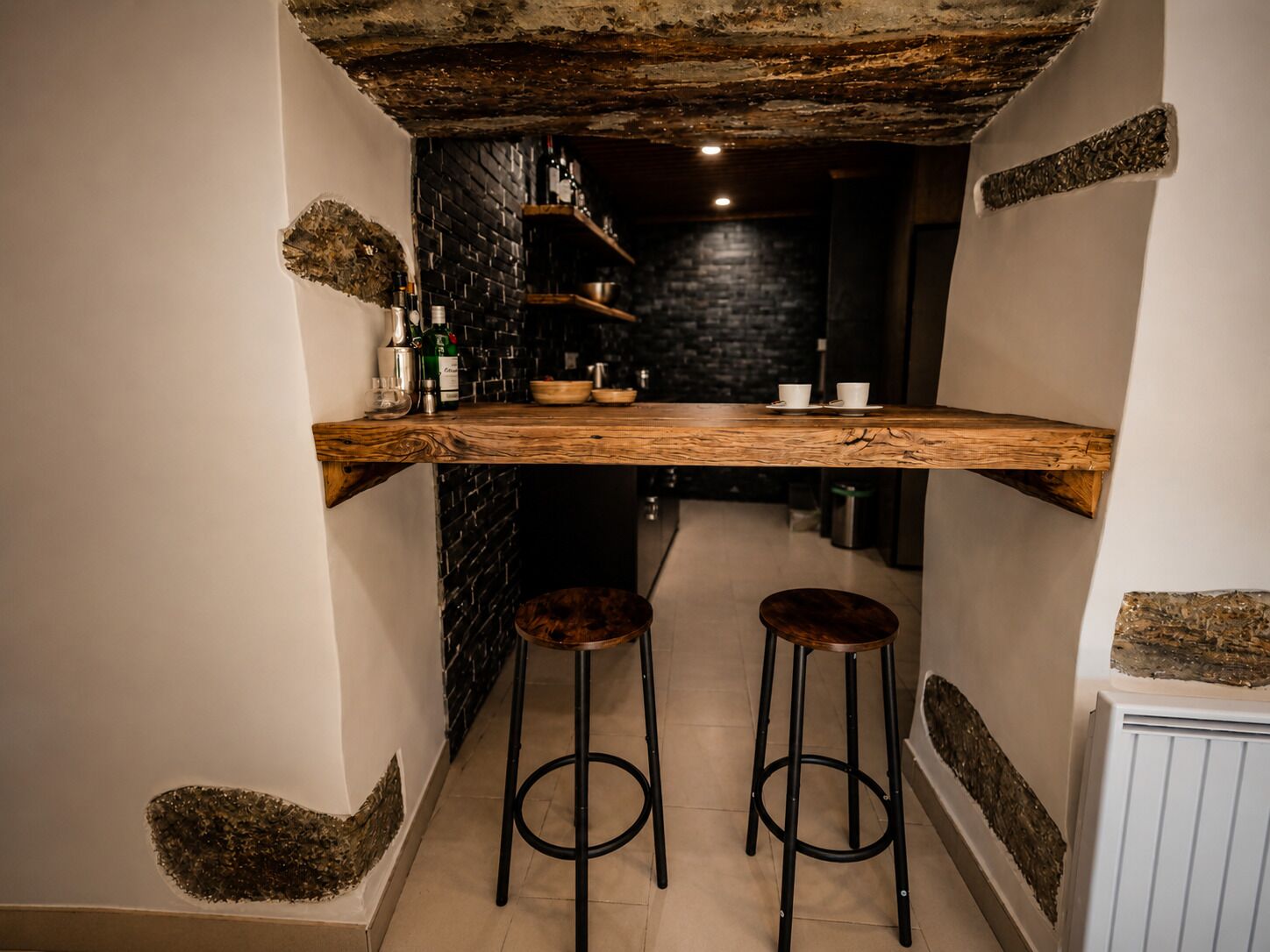 Een smalle keuken met een houten bar, twee krukken en een zwart bakstenen muur.