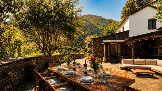 Un espace de restauration en plein air, agrémenté d’un mur en pierre, d’une table en bois et de chaises, offrant une vue sur un paysage montagneux.
