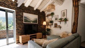Un salon avec un mur en pierre, un téléviseur à écran plat, un canapé gris et une grande fenêtre.