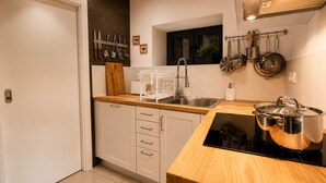 Une cuisine moderne avec des armoires blanches, un plan de travail en bois, une cuisinière encastrée et divers ustensiles de cuisine accrochés au mur.
