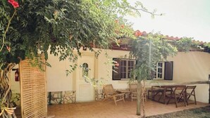Un patio con mesa y sillas, una zona cubierta y una pared con ventanas.