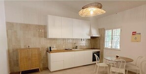 A kitchen with white cabinets, a wooden cabinet, a sink, a stove, and a dining table with chairs. - Quinta da Vala - Veranda Suite 4 (Porches)