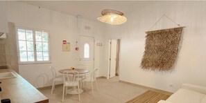 A room with a dining table, chairs, a hanging light fixture, a woven wall hanging, and a door. - Quinta da Vala - Veranda Suite 4 (Porches)