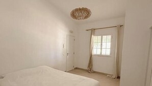 Un dormitorio con cama, ventana con cortinas y lámpara colgante.