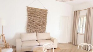 Una sala de estar con un sofá, un adorno colgante tejido en la pared, una puerta y una ventana con cortinas.