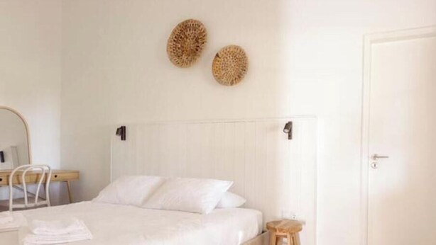 Un dormitorio con una cama, una silla, un taburete pequeño, una puerta y dos elementos decorativos en la pared.
