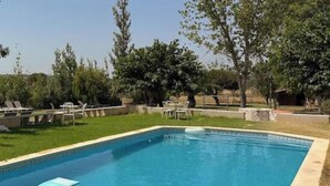 Piscina con sillas de descanso, rodeada de árboles y un cielo despejado.