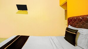 A bed with a headboard, a bedside table, a wall-mounted TV, and a window with a yellow wall. - Inviting Standard DBL Stay W/wifi Parking Access (Surabaya)