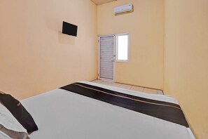 Une pièce comprenant un lit, une fenêtre fermée par un volet, un appareil de climatisation et un petit objet fixé au mur.