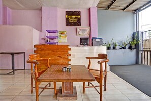 Un espace d’accueil comprenant un comptoir de réception en bois, deux chaises en bois, un sol carrelé et un mur sur lequel est affiché un panneau indiquant « Résidence Canuwa, conforme à la charia ».