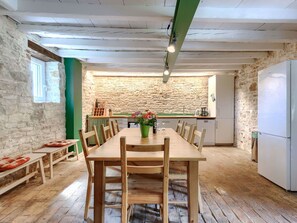 Eine rustikale Küche mit Steinwand, Holztisch, Stühlen und einem Kühlschrank.