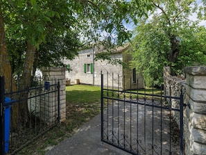 Ein Steinhaus mit einem gepflasterten Innenhof, einem Metallgitter und einem von Bäumen gesäumten Eingang.