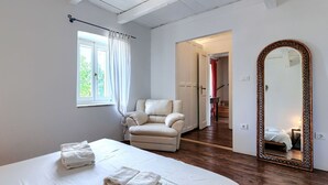 Et soveværelse med seng, stol, et stort spejl og udsigt til en trappe.