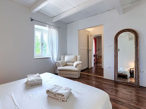 Ein Schlafzimmer mit Bett, einem Sessel, einem großen Spiegel und Blick auf eine Treppe.
