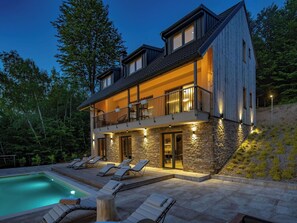 Ein modernes, zweigeschossiges Haus mit Naturstein-Fassade, einem Balkon mit Sitzgelegenheit und einem Swimmingpool.