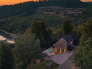Ein modernes Haus mit Swimmingpool, umgeben von dichtem Wald und Hügeln.
