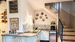 Une cuisine dotée d’un îlot central, de meubles blancs, d’un pare-feu en carrelage et d’un escalier menant à un palier.