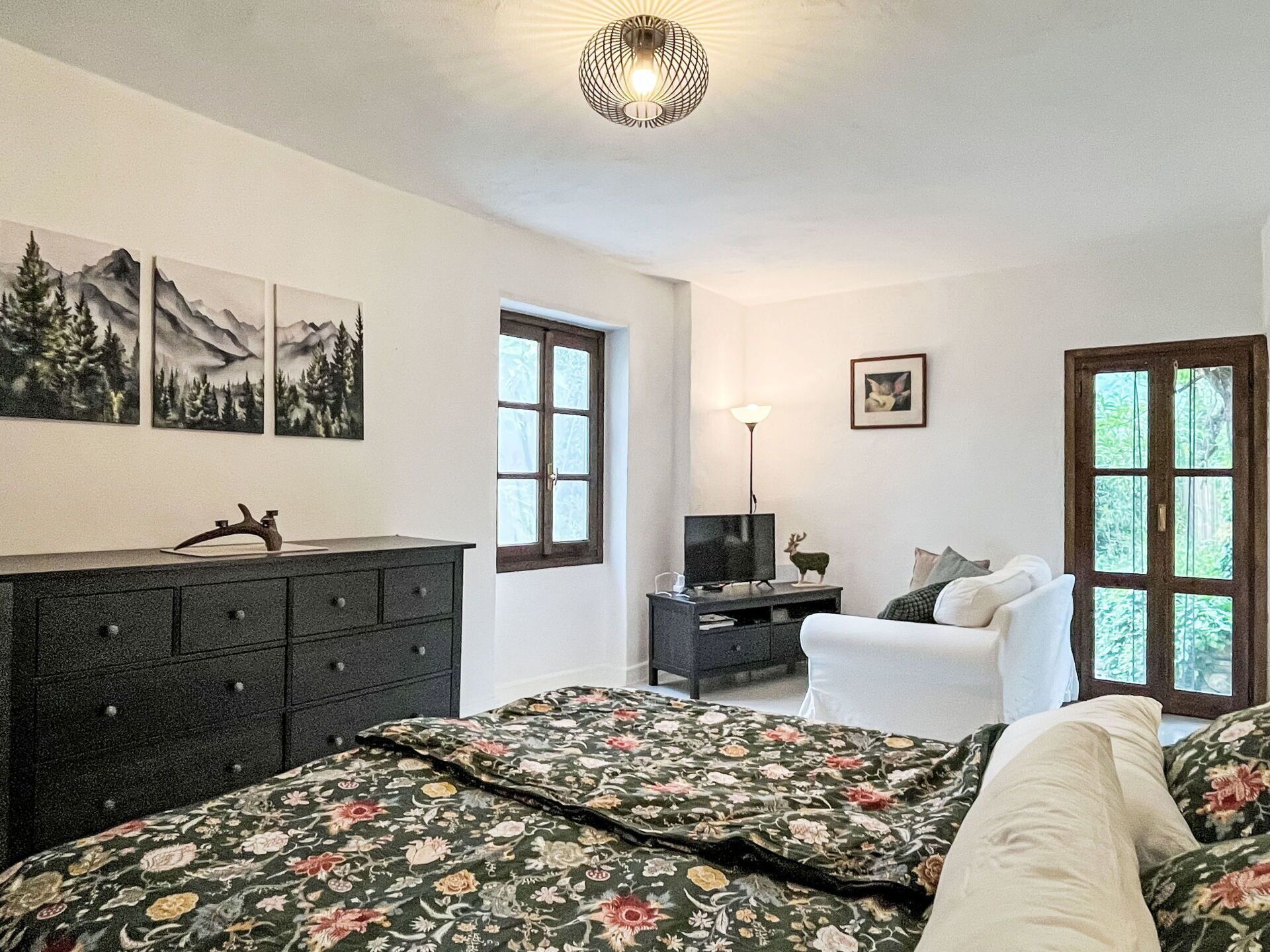 Un dormitorio con cama, cómoda, televisión y una obra de arte en la pared.