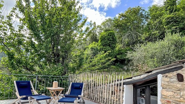 Une terrasse avec deux fauteuils bleus et une petite table, entourée d’une clôture en bambou et d’une végétation luxuriante.