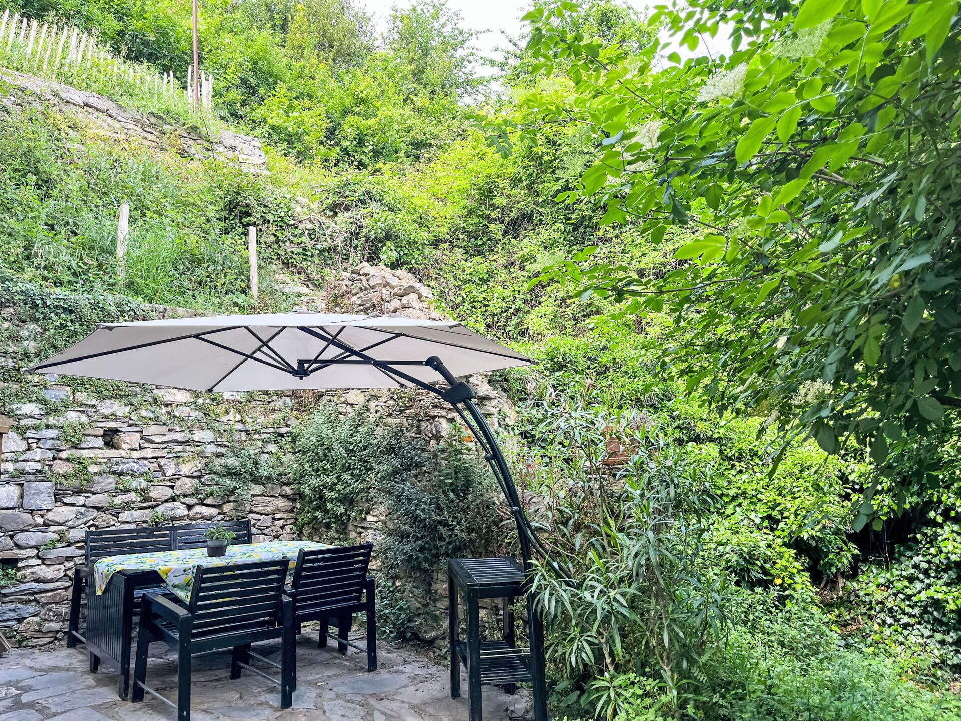 Une terrasse extérieure avec une table et des chaises, un mur en pierre et un grand parasol.