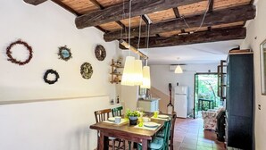 Un coin repas avec une table et des chaises en bois, un luminaire suspendu et une cuisine en arrière-plan.