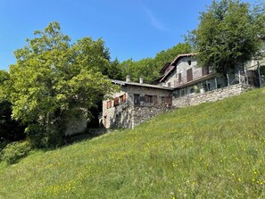 Ein Steinhaus mit Balkon, umgeben von Bäumen und einer Wiese.