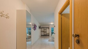Un couloir avec un mur recouvert de miroirs, une porte en bois et une vue sur une pièce où se trouvent une table et des chaises blanches.