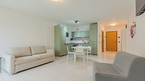 Un salon avec un canapé, une table à manger avec des chaises, un coin cuisine avec des placards et une porte donnant sur une autre pièce.