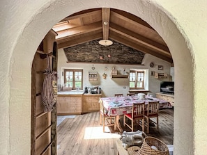 A rustic kitchen with wooden beams, a stone wall, and a dining area with a table set for four.