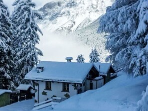 A snow-covered mountain landscape with a house and trees.