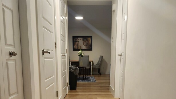 Un corridoio con pavimento in legno, porte bianche e un'area da pranzo sullo sfondo.