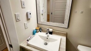 Un bagno con un lavandino bianco, uno specchio con cornice a spina di pesce, un water e un cestino.